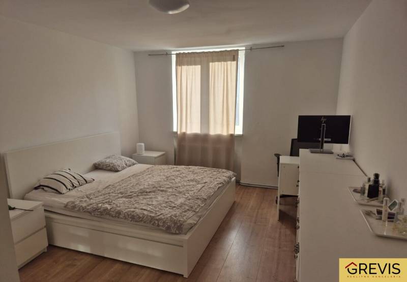 Világos hálószoba egy háromszobás lakásban, ággyal és fa mintázatú padlóval.