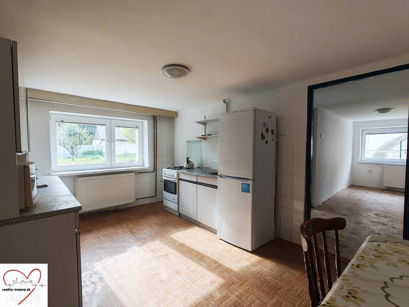 Családi ház konyhája fa mintázatú padlóval, felszerelve háztartási gépekkel és étkezőasztallal.