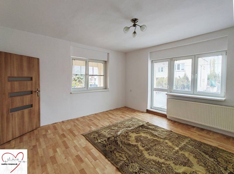 Szoba egy családi házban, fa mintázatú padlóval, szőnyeggel és nagy ablakkal.