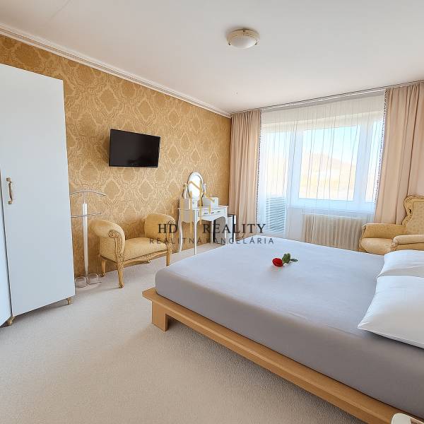 Hálószoba egy háromszobás lakásban elegáns bútorokkal, arany tapétával és fehér szőnyeggel.