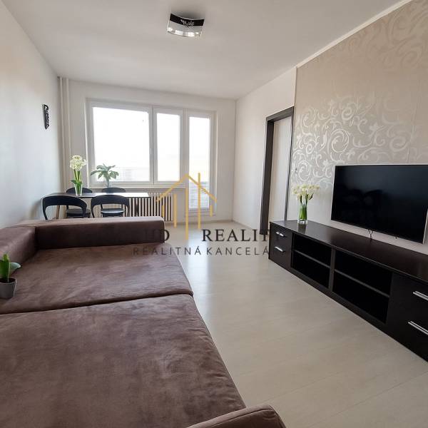 Nappali egy háromszobás lakásban nagy kanapéval, TV-vel és fa mintázatú padlóval.