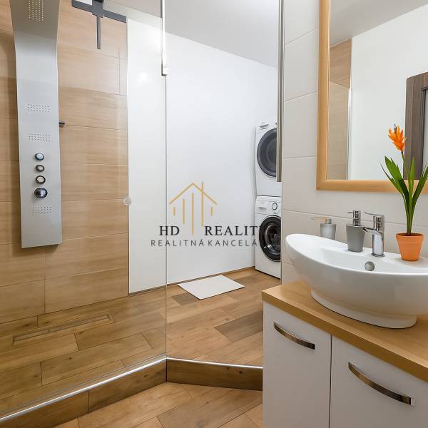 Fürdőszoba egy háromszobás lakásban mosdóval, zuhanyzóval és mosógéppel, fa dekoros padlóval.