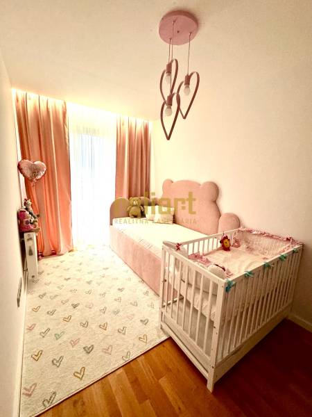 Gyerekszoba egy háromszobás lakásban rózsaszín részletekkel és fa padlóval.