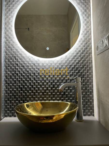 Kerek megvilágított tükör és arany mosdókagyló egy háromszobás lakásban.