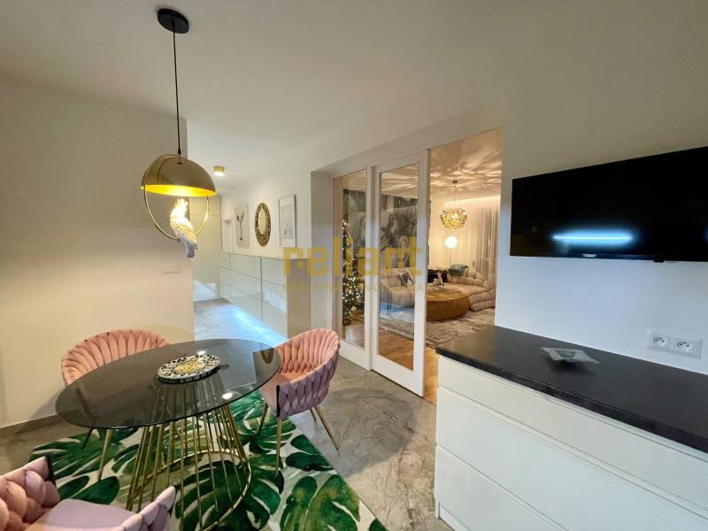 Étkező sarok kerek asztallal, rózsaszín székekkel és érdekes világítással egy háromszobás lakásban.