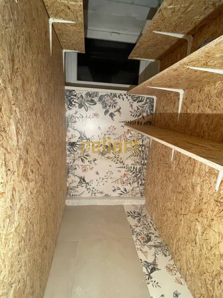 Tárolóhely egy háromszobás lakásban fa polcokkal és virágos tapétával.