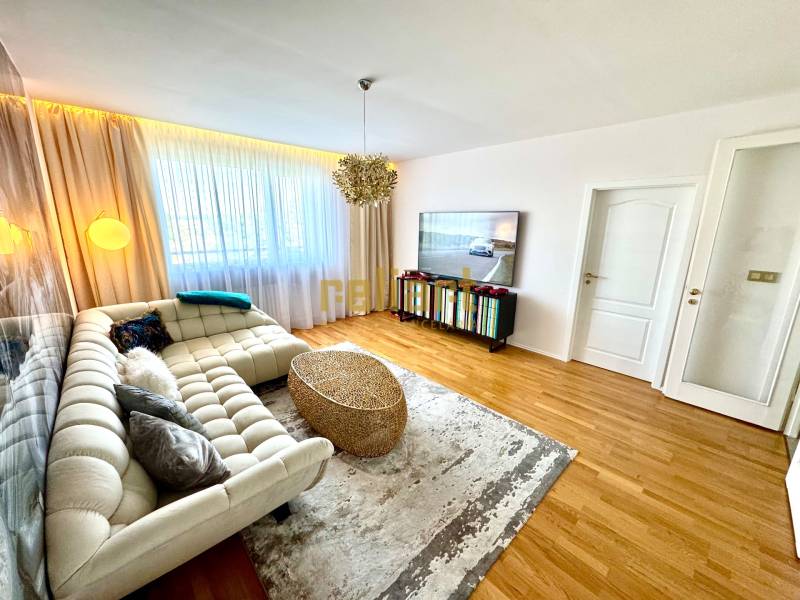 Nappali háromszobás lakásban kanapéval, televízióval és függönyökkel az ablakon.