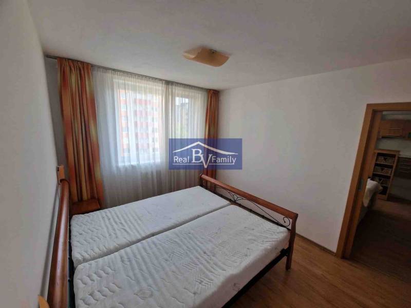 Hálószoba egy kétszobás lakásban ággyal, függönyökkel és fa dekorációjú padlóval.