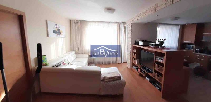 Nappali fehér kanapéval és televízióval, fa hatású padlóval, 2 szobás lakás.