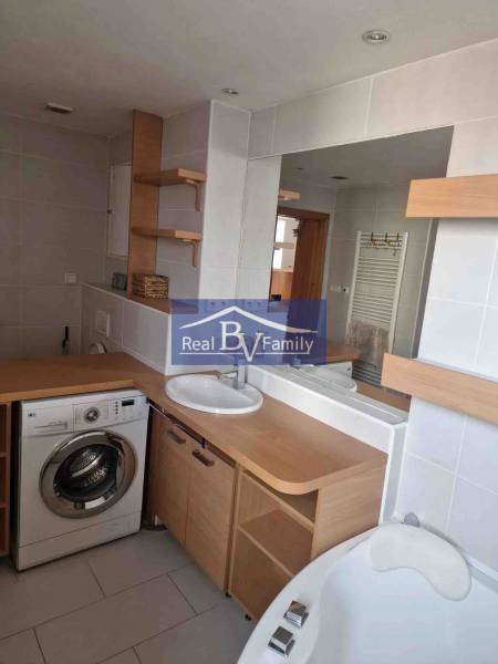 Fürdőszoba egy kétszobás lakásban mosógéppel, mosdóval és káddal, fa dekorációval felszerelve.