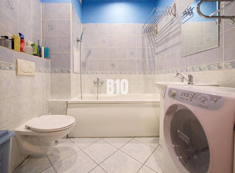 Fürdőszoba egy kétszobás lakásban zuhanyzóval, mosdóval és mosógéppel.