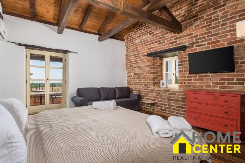 Hálószoba egy villában téglafalakkal, TV-vel, kanapéval és nagy ággyal.