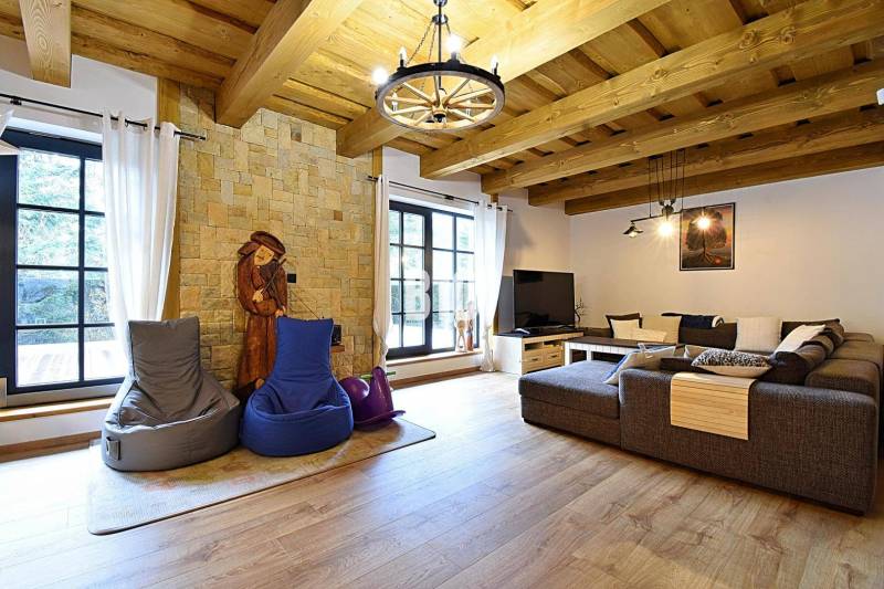 Hegyi ház belső tere kőfallal, nagy kanapéval és fa dekorációjú padlóval.