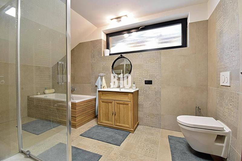 Fürdőszoba káddal, zuhanyzóval, tükörrel és szekrénnyel a házikóban. Világos csempék és padlóburkolat.