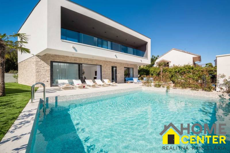 Villa Balin medencével és napozóágyakkal, zölddel és kék éggel körülvéve.