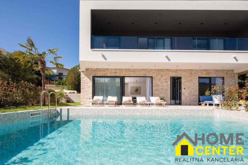 Villa medencével, pálmafákkal, terasszal és napozóágyakkal a háttérben.