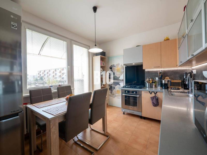 Konyha egy 4 szobás lakásban étkezőasztallal, barna székekkel és nagy ablakkal.