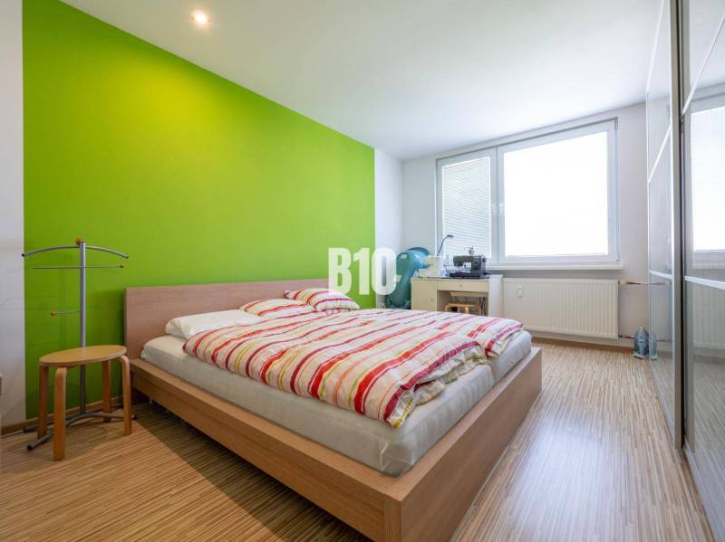 Hálószoba egy 4 szobás lakásban, fa dekoros padlóval és zöld fallal.