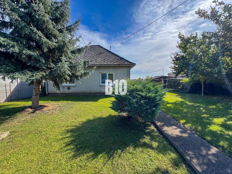 Családi ház Ondrejovcén füves kerttel, két fával és egy bokorral a járda mellett.