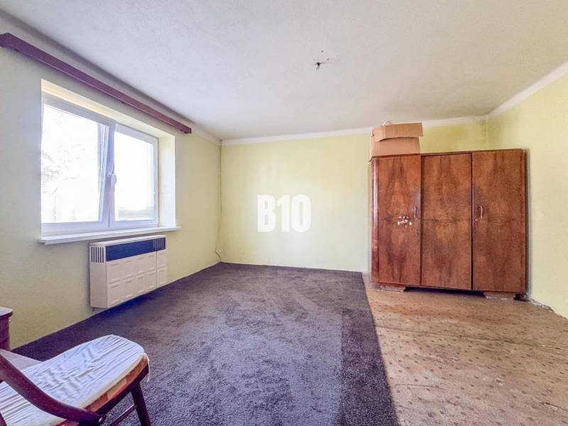 Szoba egy családi házban, szőnyeggel, régi szekrénnyel és fotellel.