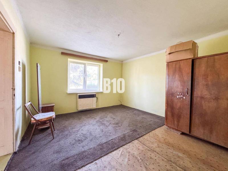 Egyszerű szoba egy családi házban, szőnyeggel és fa bútorokkal.