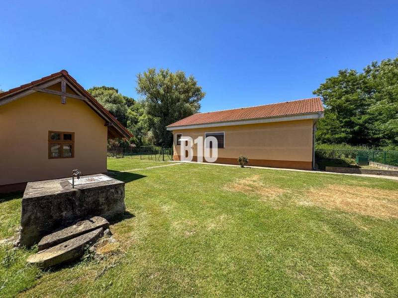 Új Szádok családi házának udvara két épülettel és kúttal, zölddel körülvéve.