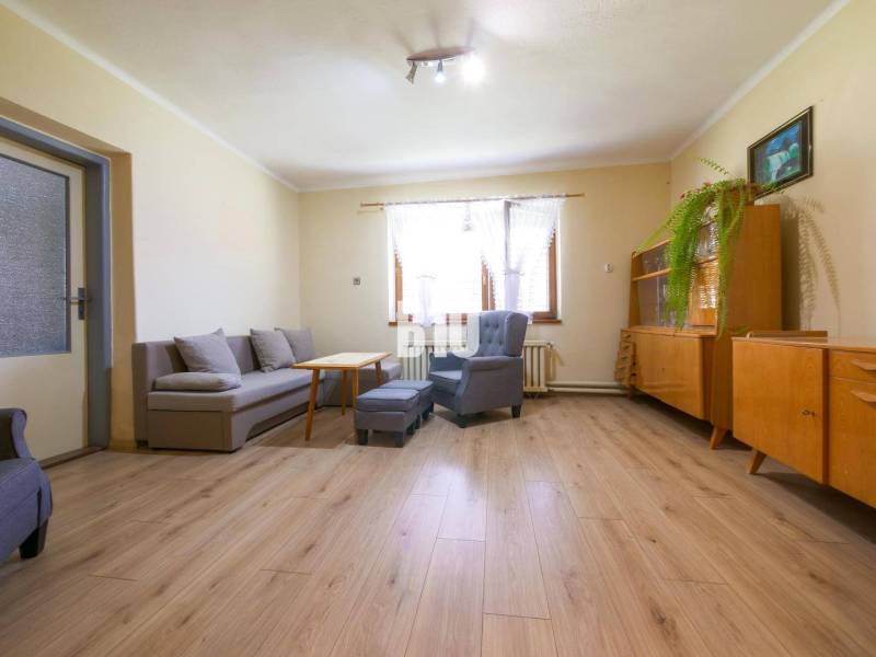 Nappali egy családi házban, fa bútorokkal, szürke kanapéval és világos padlóburkolattal.