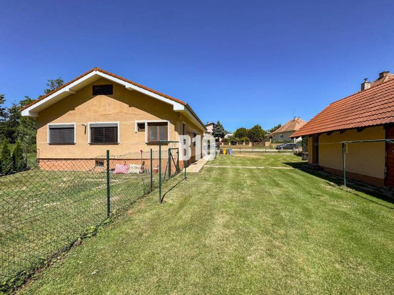 Családi ház Újszálláson két épülettel és füves telken, kerítéssel körülvéve.