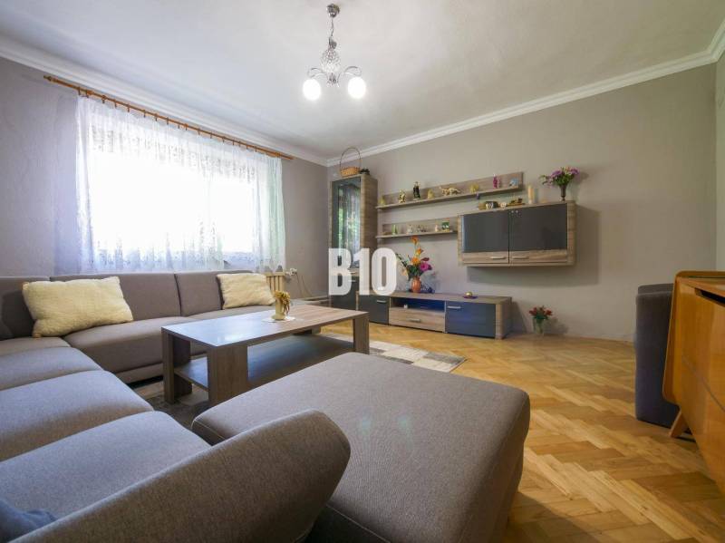 Nappali sarokkanapéval, fa parkettával, dekoratív polcokkal és világítással egy családi házban.