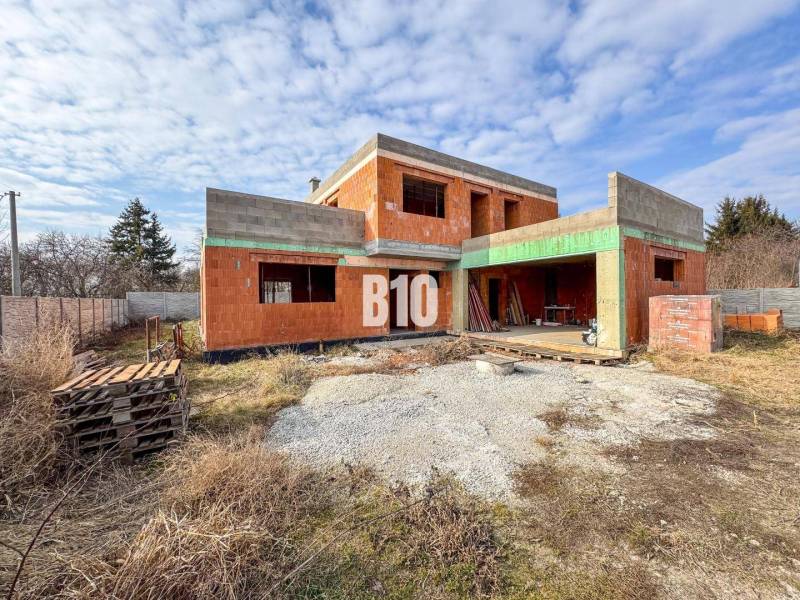 Befejezetlen téglából épült családi ház, amit fű és fa raklapok vesznek körül.