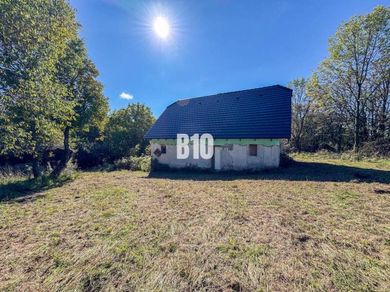 Ház Lackovban, természettel körülvéve, kék tetővel, napos nap.