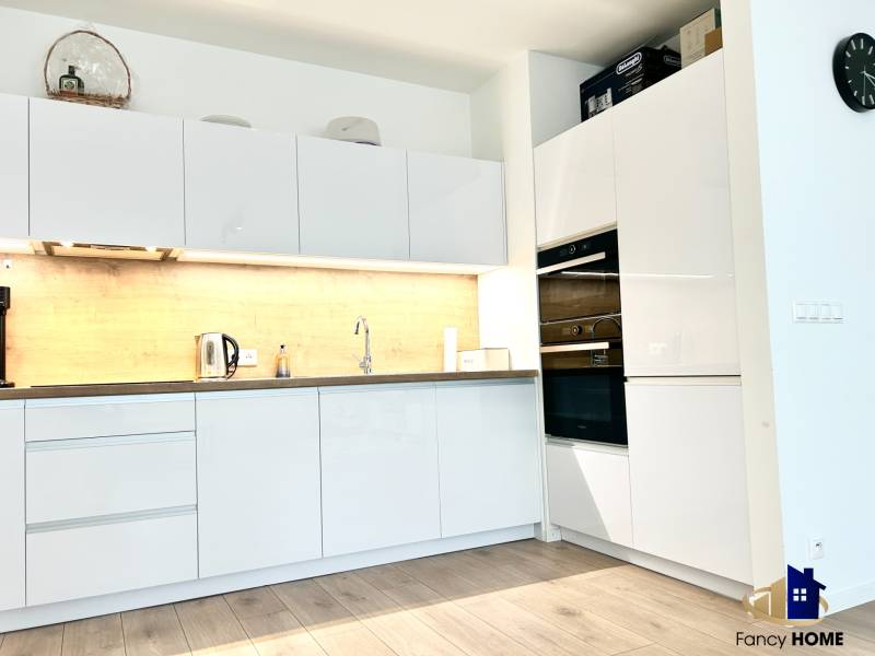 Konyha egy kétszobás lakásban fehér szekrényekkel és fa mintázatú padlóval.