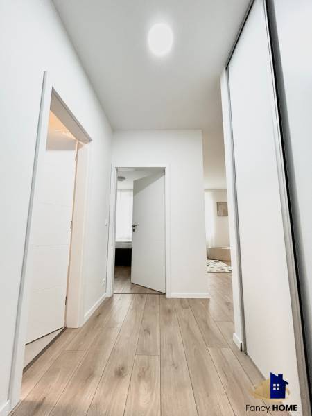 Folyosó világos falakkal és fa dekoros padlóval, amely egy kétszobás lakás helyiségeibe vezet.