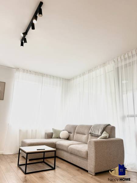 Világos szoba egy kétszobás lakásban kanapéval és fa dekor padlóval.