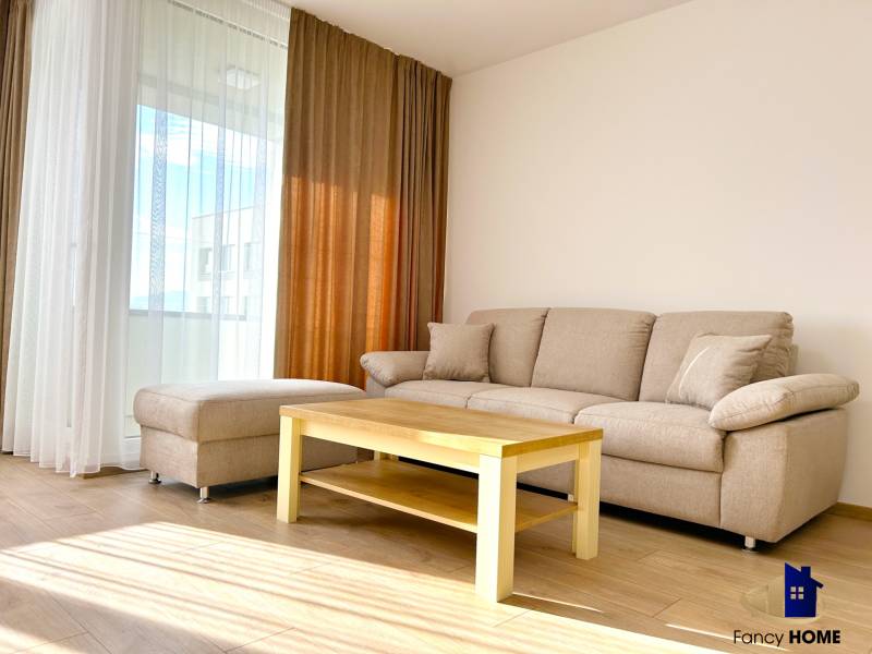 Nappali a kétszobás lakásban kanapéval, asztallal és fa dekorációjú padlóval.