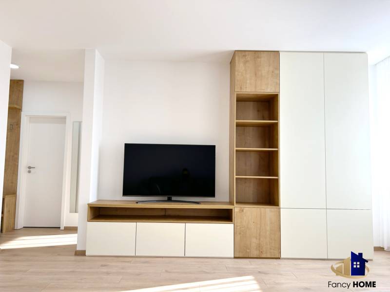 Nappali egy kétszobás lakásban, televízióval és fa dekorációjú bútorokkal.