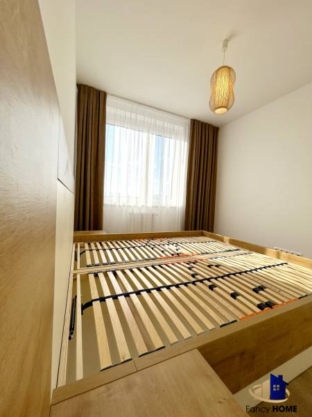 Hálószoba ággyal és lámpával egy kétszobás lakásban, fa mintázatú padlóval.