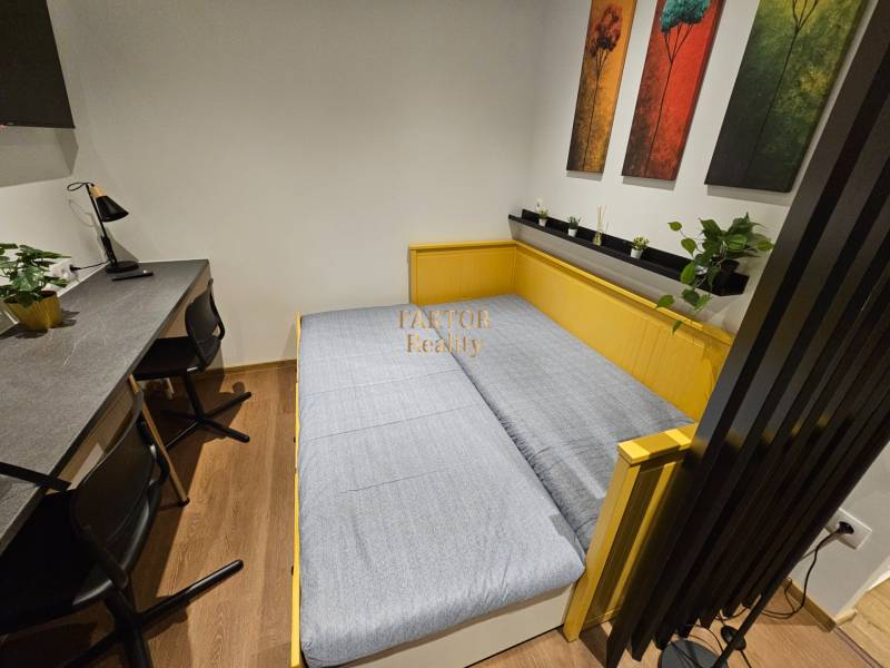 Garzonlakás ággyal, asztallal, székekkel és dekoratív képekkel, fa dekorációjú padlóval.