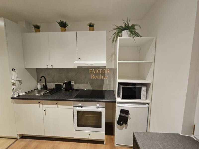 Konyha garzonlakásban fehér szekrényekkel és fa mintázatú padlóval.