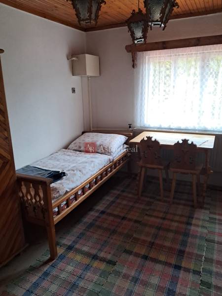 Szoba egy családi házban ággyal, ablakkal, asztallal és székekkel.