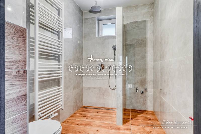 Zuhanykabin családi házban, fa mintázatú padlóval és világos csempékkel.