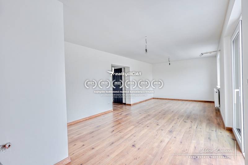 Tágas szoba egy családi házban, fa dekorációjú padlóval és fehér falakkal.