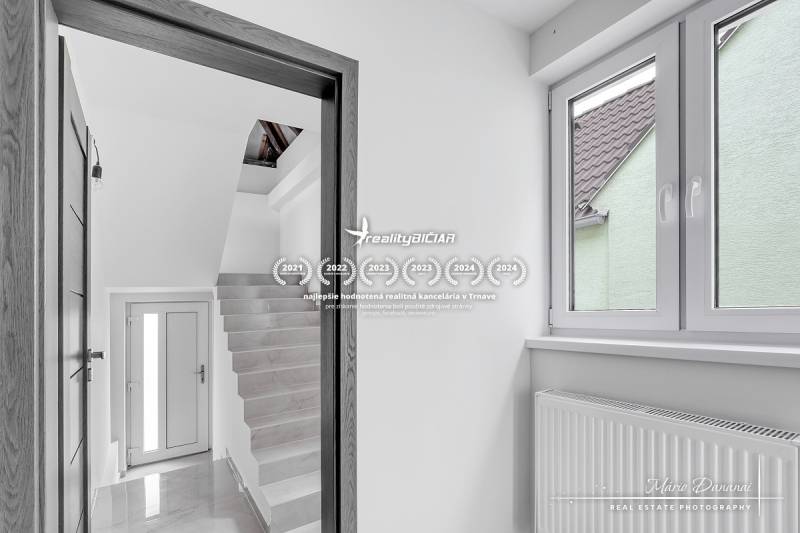 Családi ház belső tere fehér falakkal, lépcsővel és nagy ablakkal.