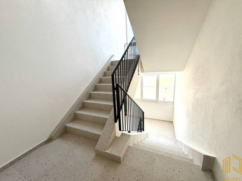 Lépcsőház egy lakóépületben ablakkal, fehér falak és csempe.