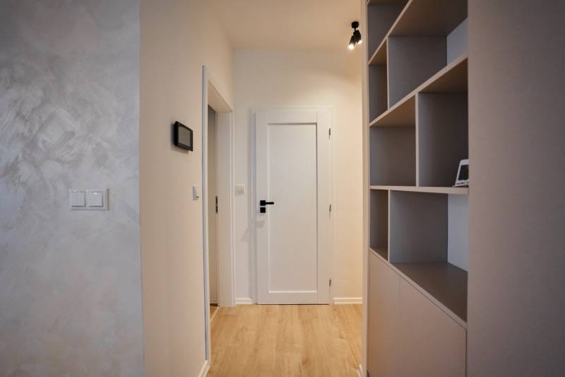 Folyosó egy 2 szobás lakásban polcos fallal és fa dekorációjú padlóval.