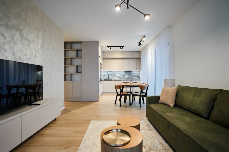 2 szobás lakás belső tere sötétzöld kanapéval, konyhával és fa mintázatú padlóval.