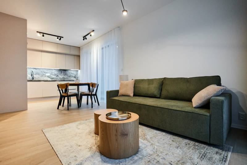 Nappali rész egy kétszobás lakásban konyhával és fa dekor padlóval, zöld kanapéval és asztallal.