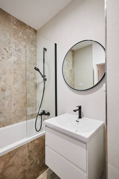 Fürdőszoba káddal, kerek tükörrel és modern mosdóval egy kétszobás lakásban.