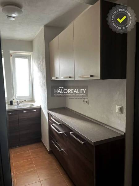 Konyha egy háromszobás lakásban sötét szekrényekkel és ablakkal.