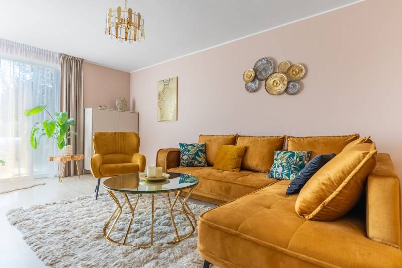 Nappali egy családi házban mustársárga kanapéval és fa dekorációjú padlón lévő asztallal.